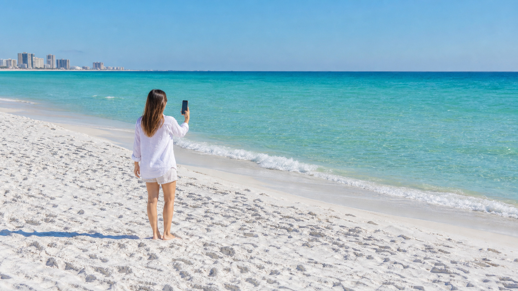 Person checking cell phone signal on Destin Florida beach with emerald Gulf water behind them on a sunny day