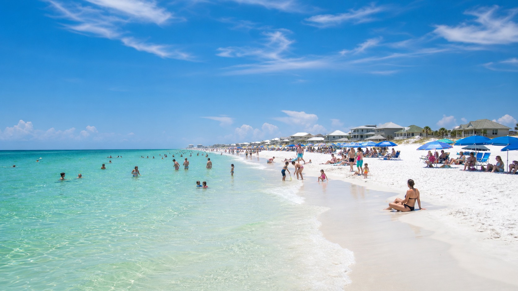 Families swimming and relaxing on the sugar-white beach in Destin Florida with emerald green Gulf water on a sunny summer afternoon