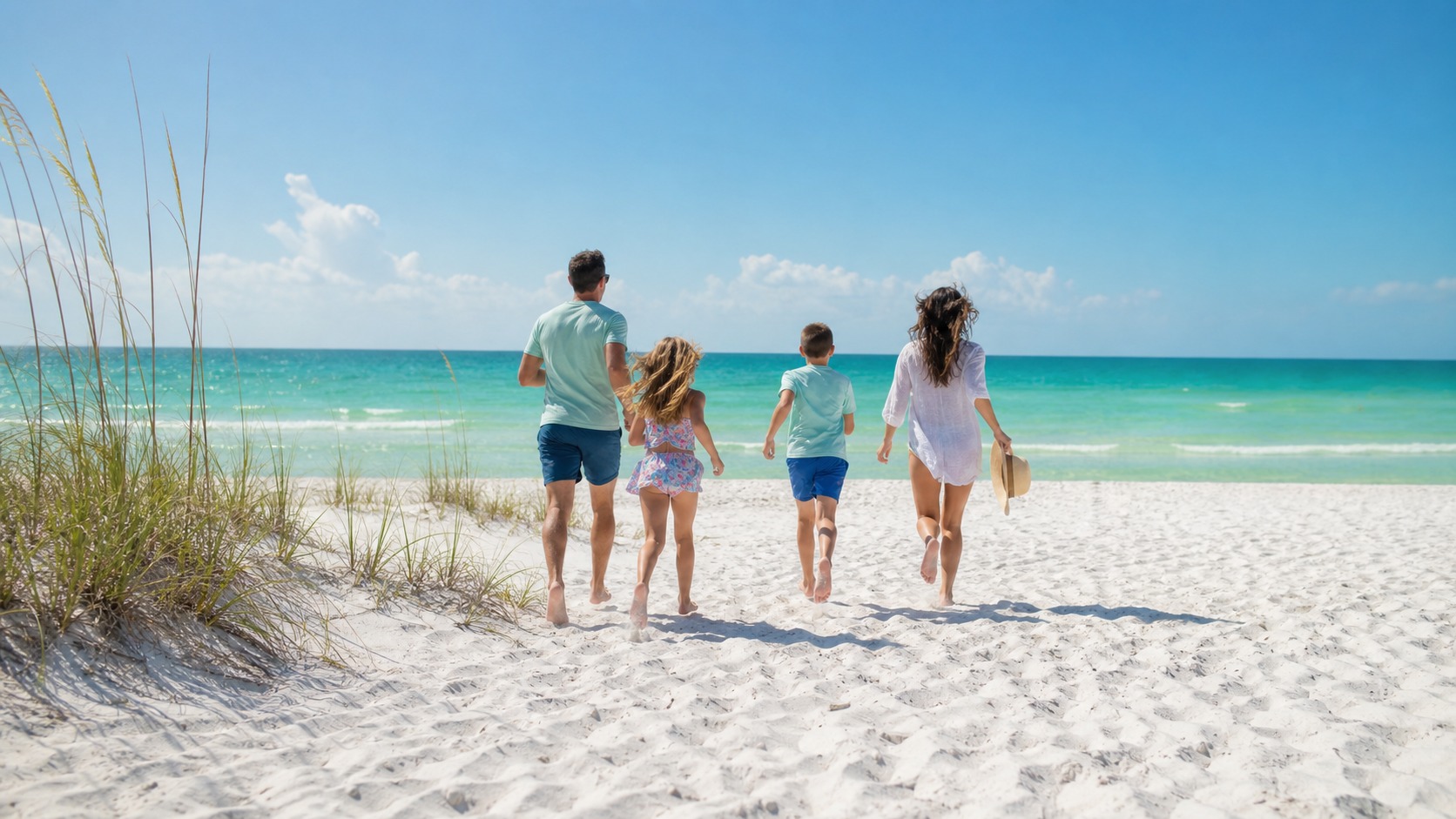 Happy family of four running toward the emerald green Gulf of Mexico on a white sand beach in Destin Florida on a sunny summer morning
