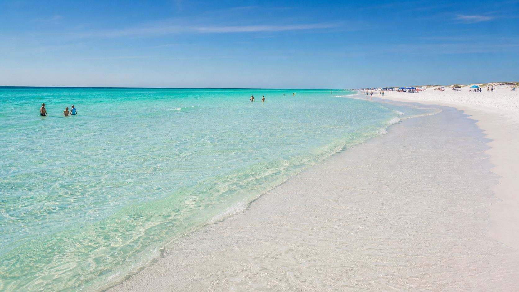 Crystal-clear emerald-green water at Destin Florida beach with brilliant white quartz sand, shallow waves and families wading in the Gulf