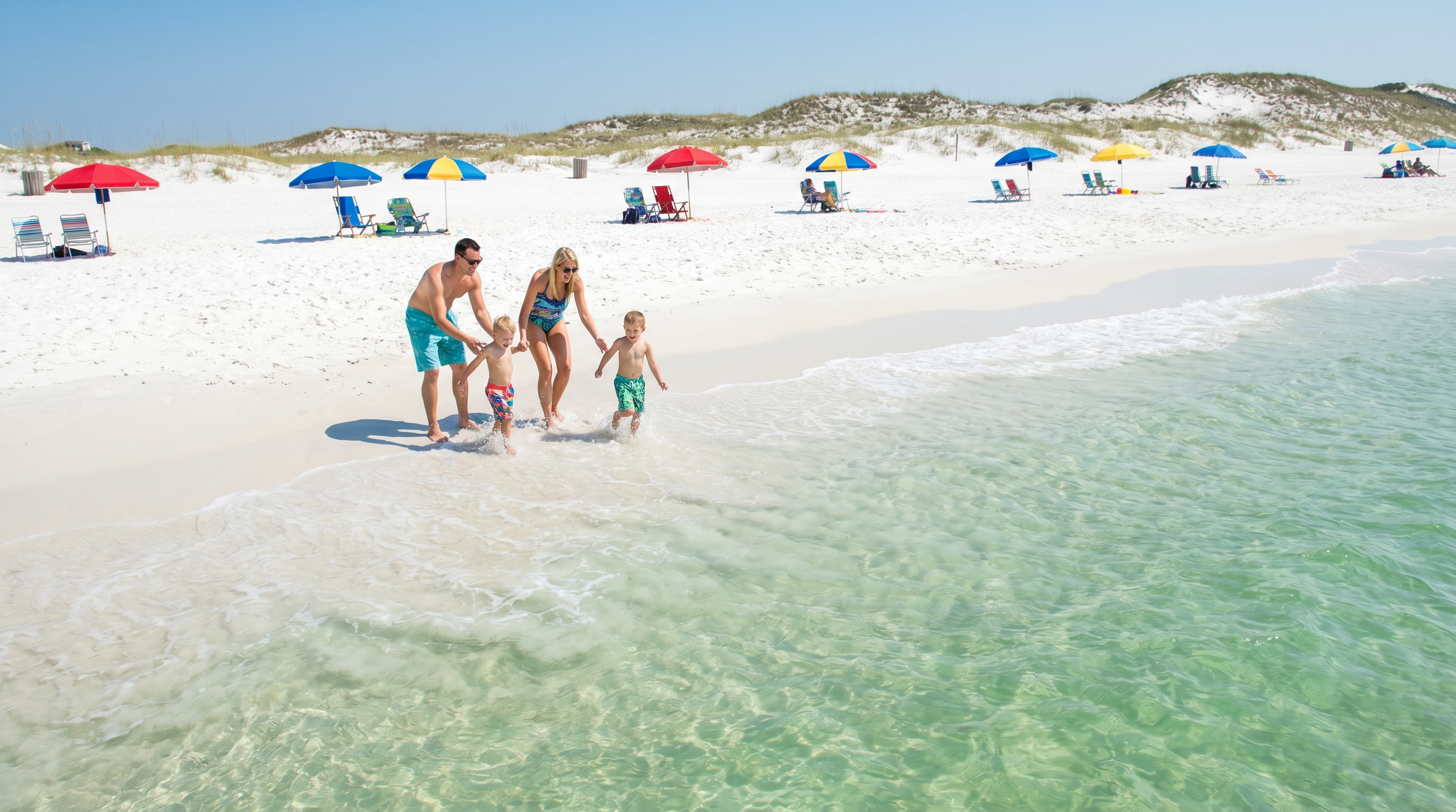 White sugar sand beach with emerald Gulf water in Destin Florida on a sunny summer day with families and colorful umbrellas
