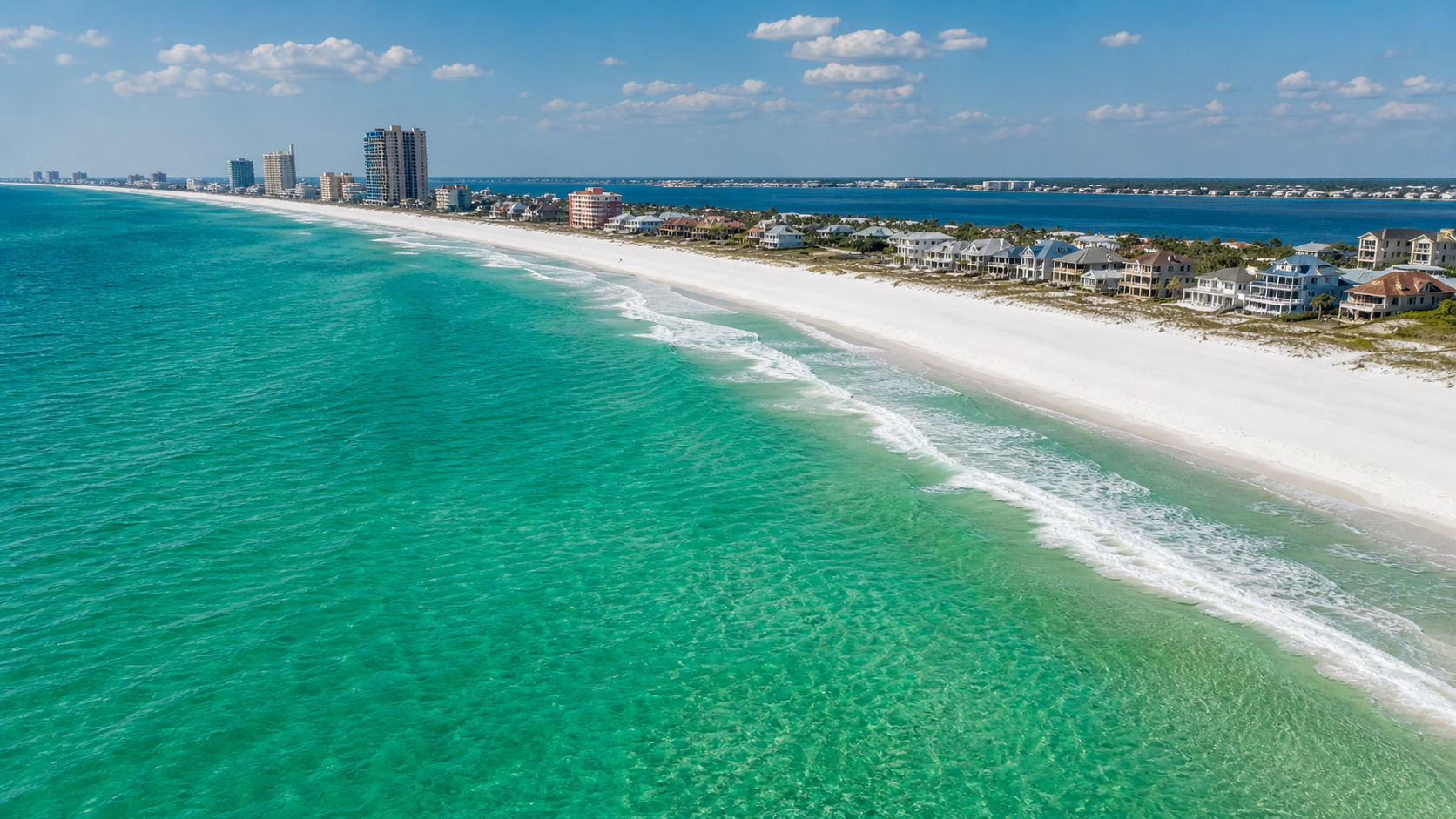 Aerial view of Destin Florida's emerald green Gulf water and white quartz sand beach with turquoise surf on a sunny summer day