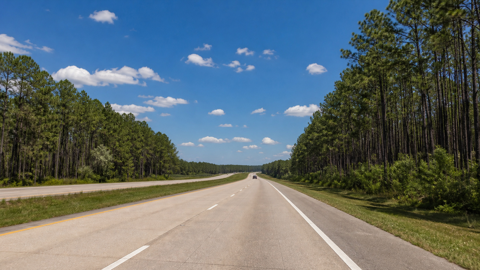 Open highway road trip through the Florida Panhandle with pine forests flanking both sides of the interstate under a clear blue summer sky