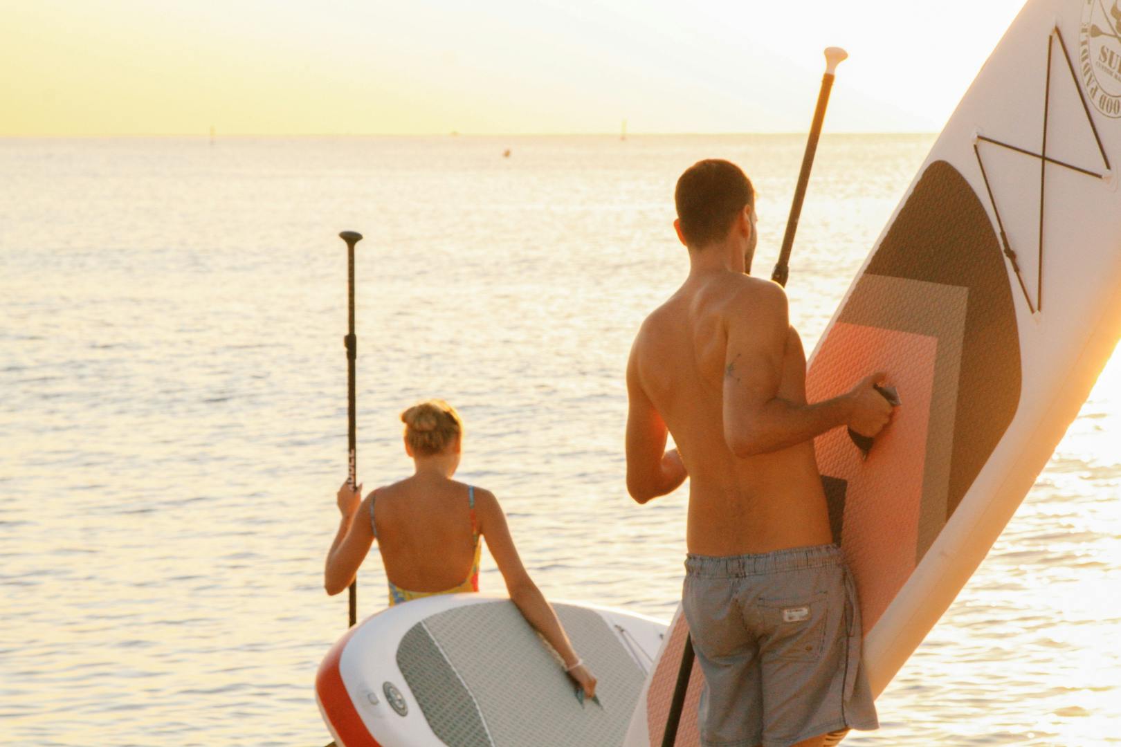 Couple paddleboarding on perfectly calm glassy bay water near Miramar Beach Florida at golden hour