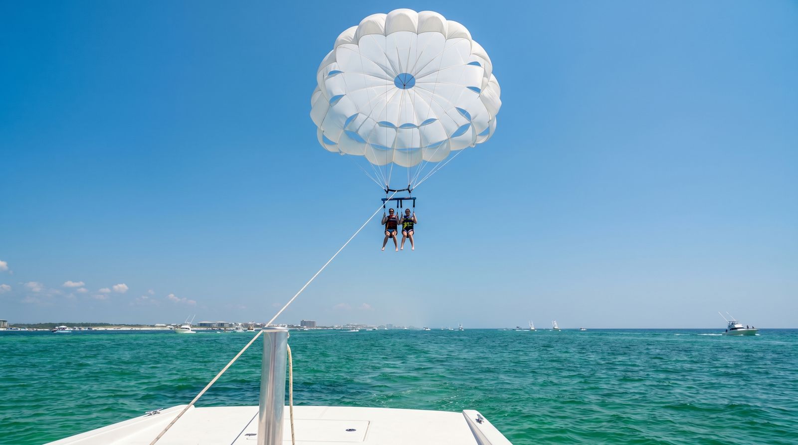 Couple parasailing high above the emerald green Gulf of Mexico near Destin Florida on a bright clear day with charter boats below
