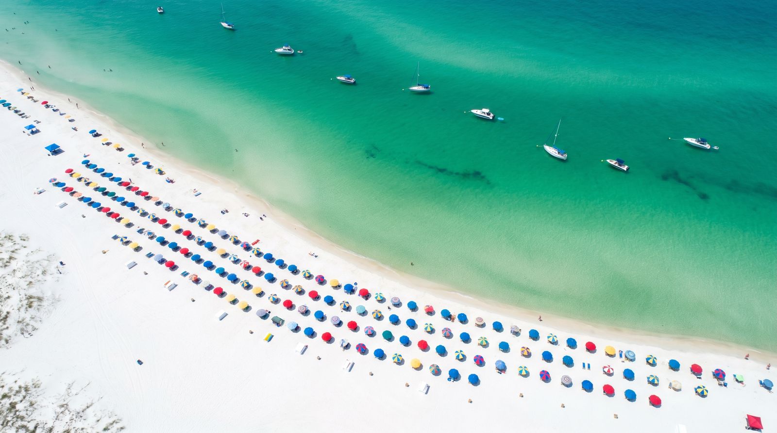 Aerial view along the white sand beaches of Destin Florida stretching into the distance with emerald Gulf water and beach umbrellas