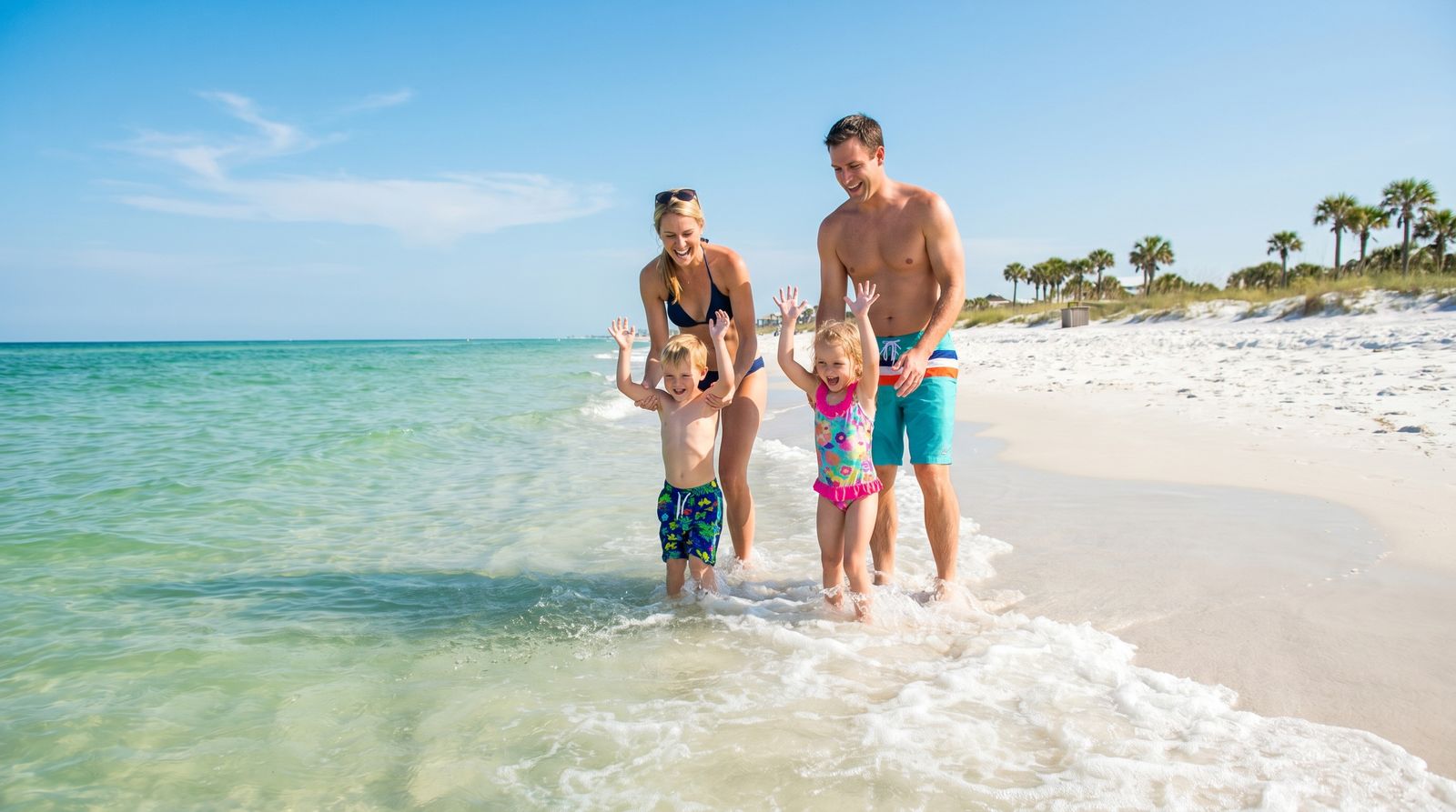 Happy family with two young children splashing and playing in shallow turquoise Gulf water on a white sand Florida beach on a sunny day