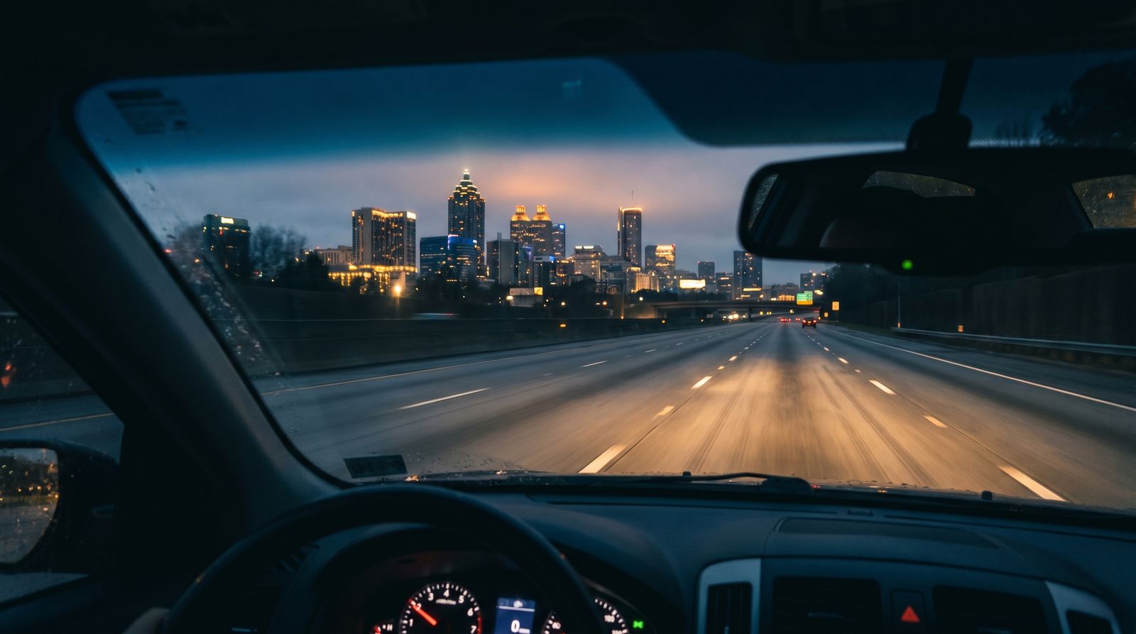 Pre-dawn view from inside a car on an empty Atlanta interstate highway with the city skyline glowing ahead, early morning departure for a beach road trip