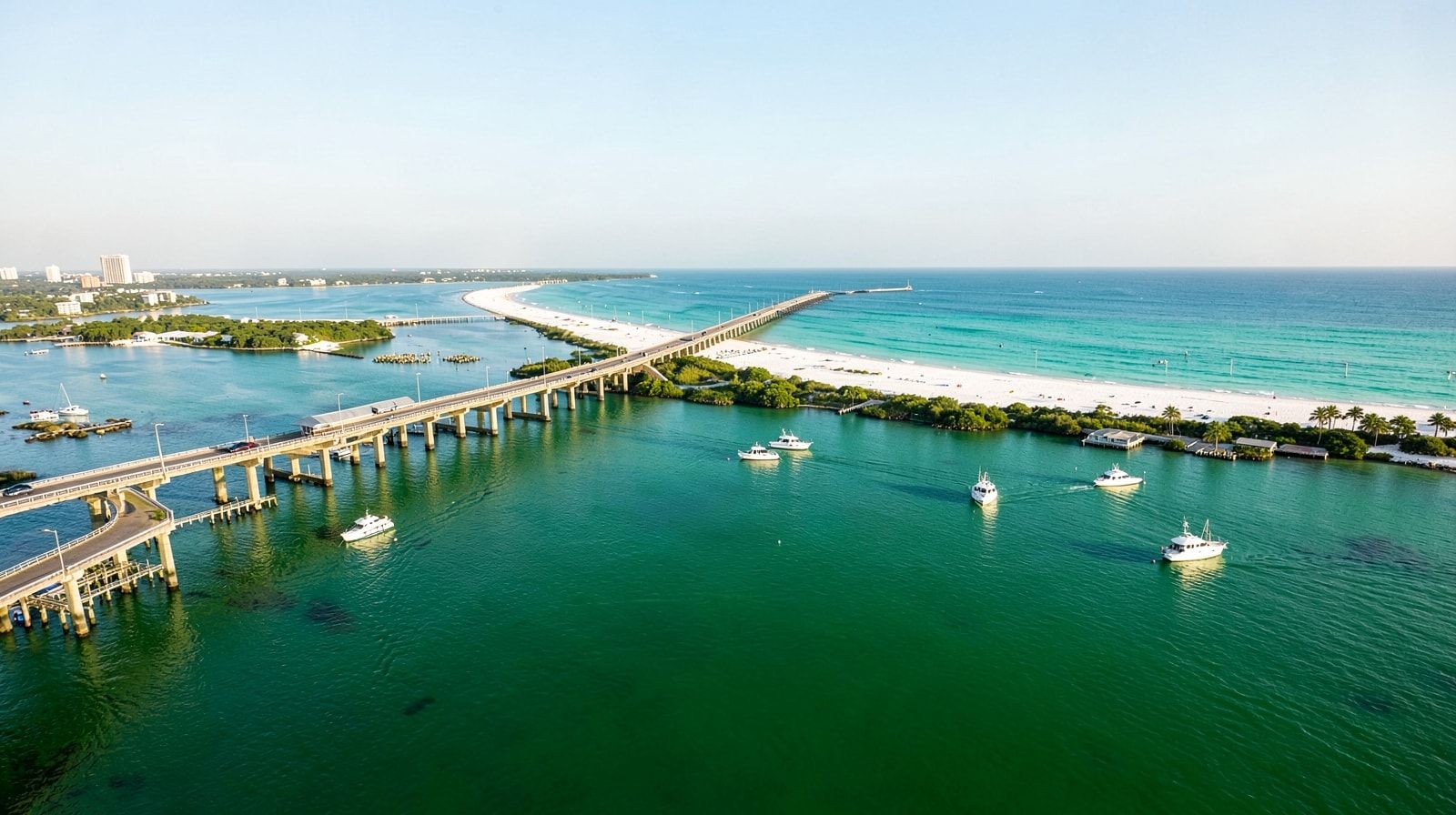 View from the Destin bridge looking over the emerald green harbor, white sand beaches visible beyond, charter fishing boats in calm water, morning light