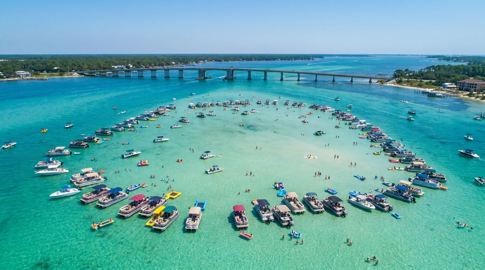 Group of young adults swimming and wading at Crab Island in Destin Florida with pontoon boats anchored in emerald green shallow water